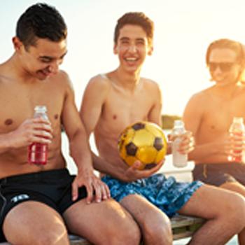 Boys in swim trunks sitting on bench with drink bottles